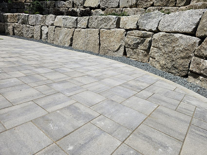 New granite boulder retaining wall and curved paver patio installed in a Twin Cities backyard by Triple Landscaping