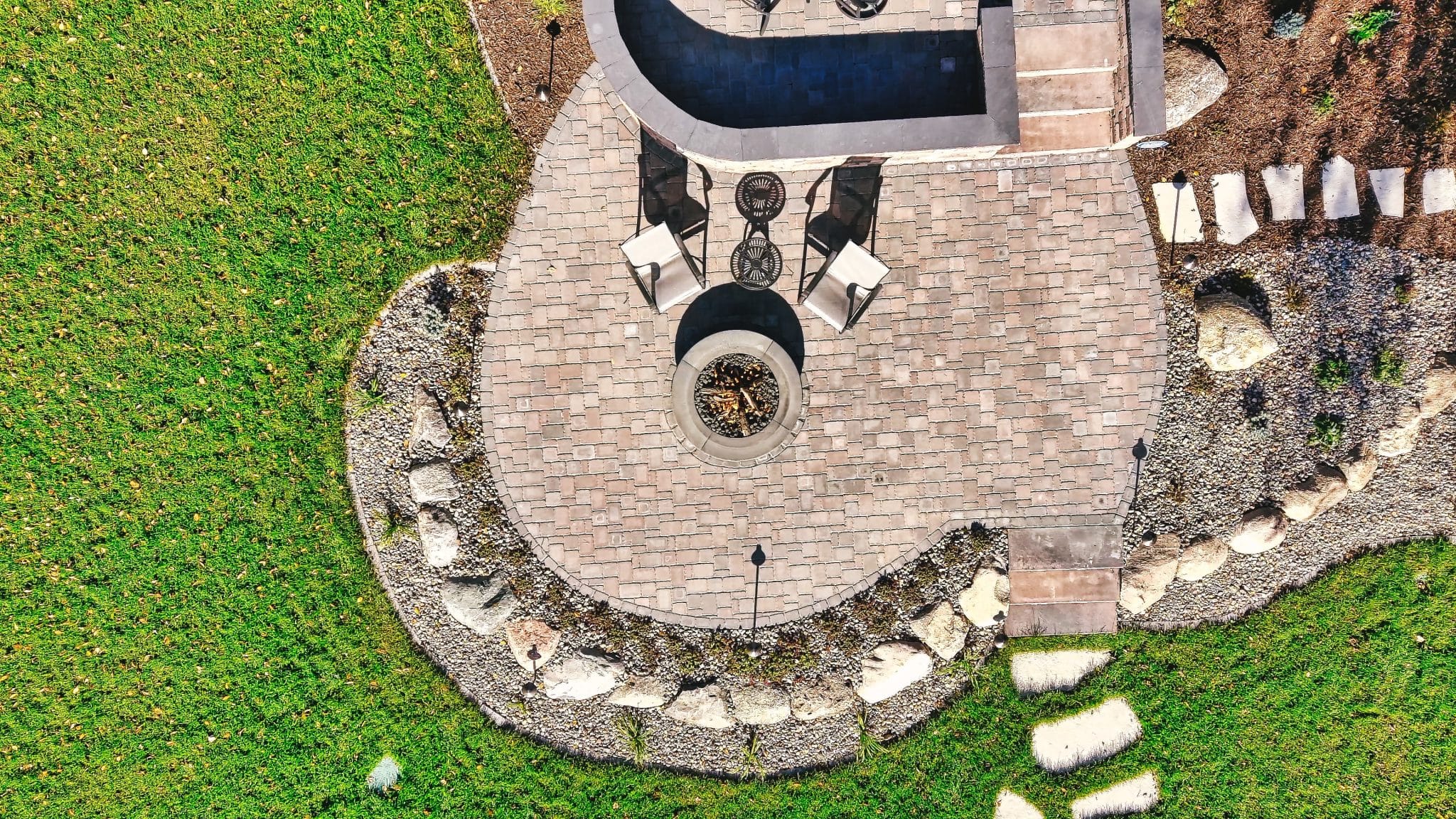 Aerial drone view of a circular paver patio with fire pit and boulder border installed by Triple Landscaping
