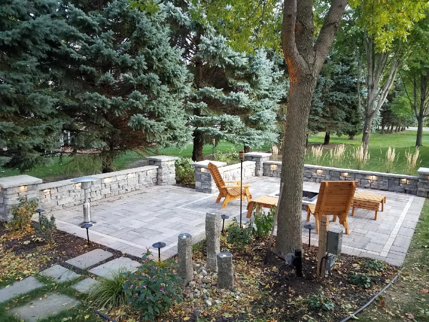 Stone retaining wall with LED lighting enclosing a paver patio surrounded by mature trees in a Twin Cities backyard